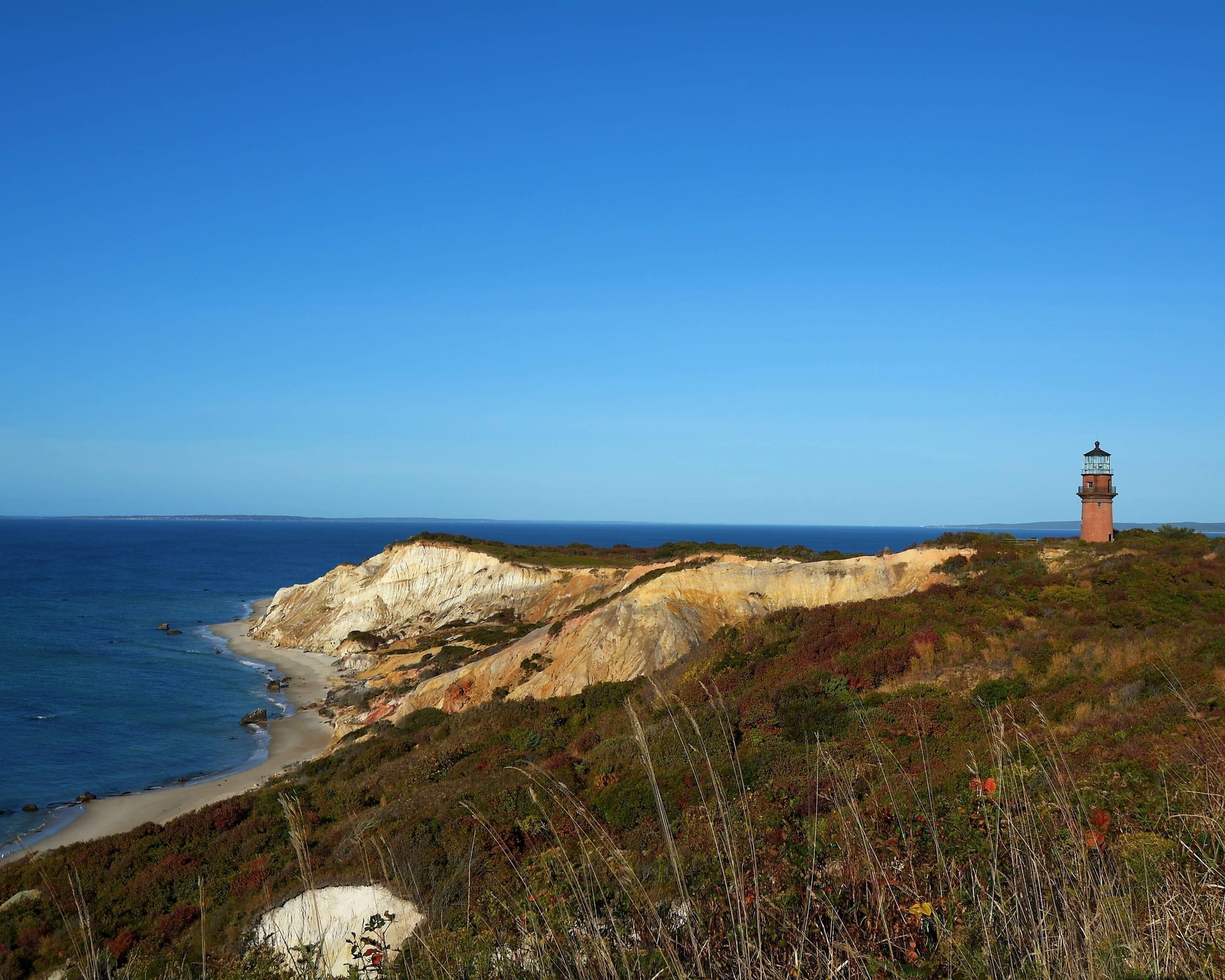 Un paisaje costero con un faro en una colina, con vistas a una playa y acantilados.
