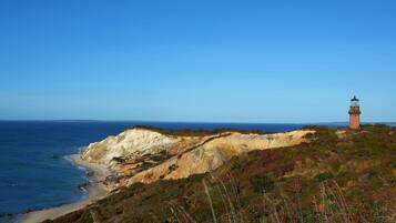 Un paisaje costero con un faro en una colina, con vistas a una playa y acantilados.