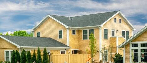 A two-story house with a wooden exterior, a fenced yard, and a clear sky.