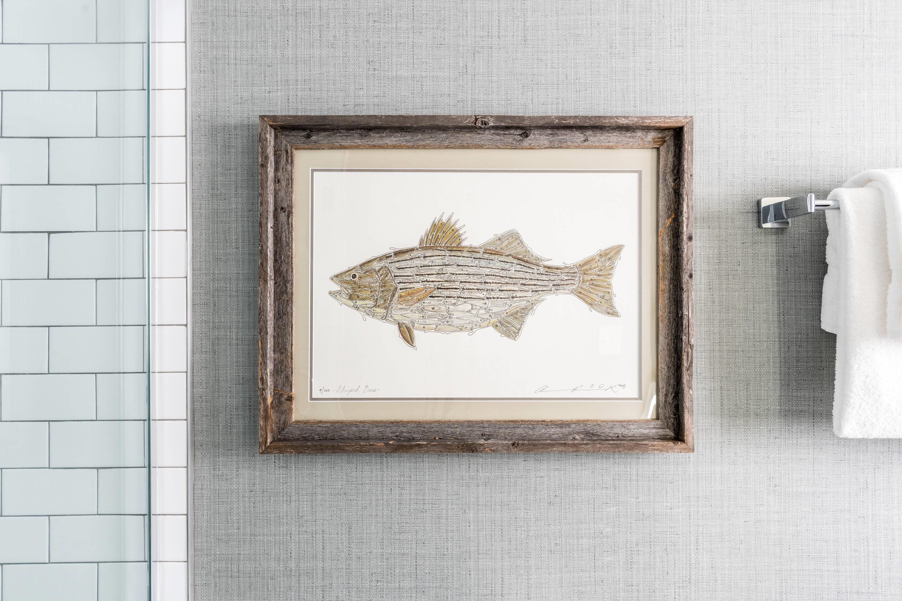 A framed fish artwork on a textured wall, a white towel on a metal towel rack, and a white tiled backsplash.
