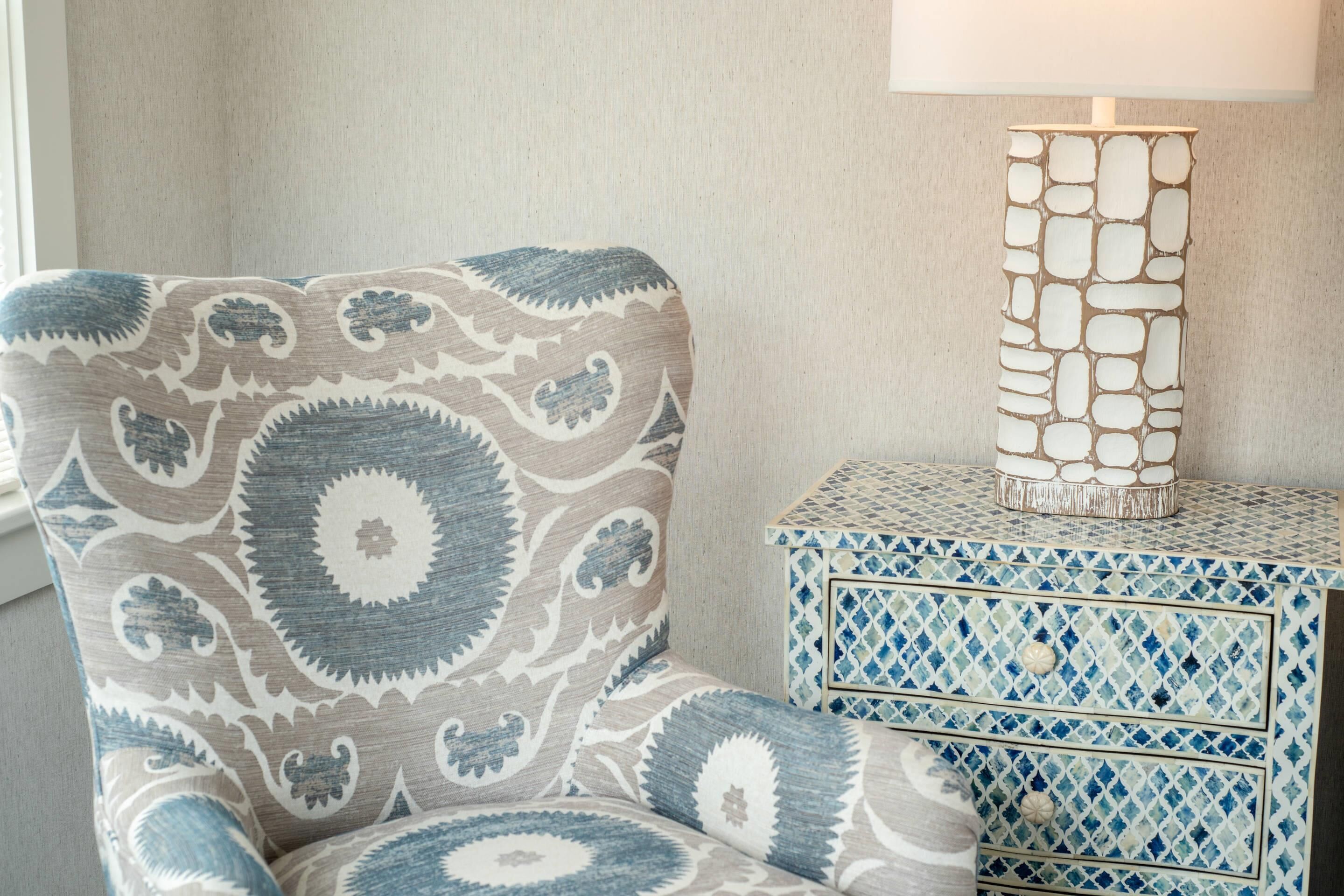 A patterned armchair, a decorative lamp, and a tiled storage unit in a room.