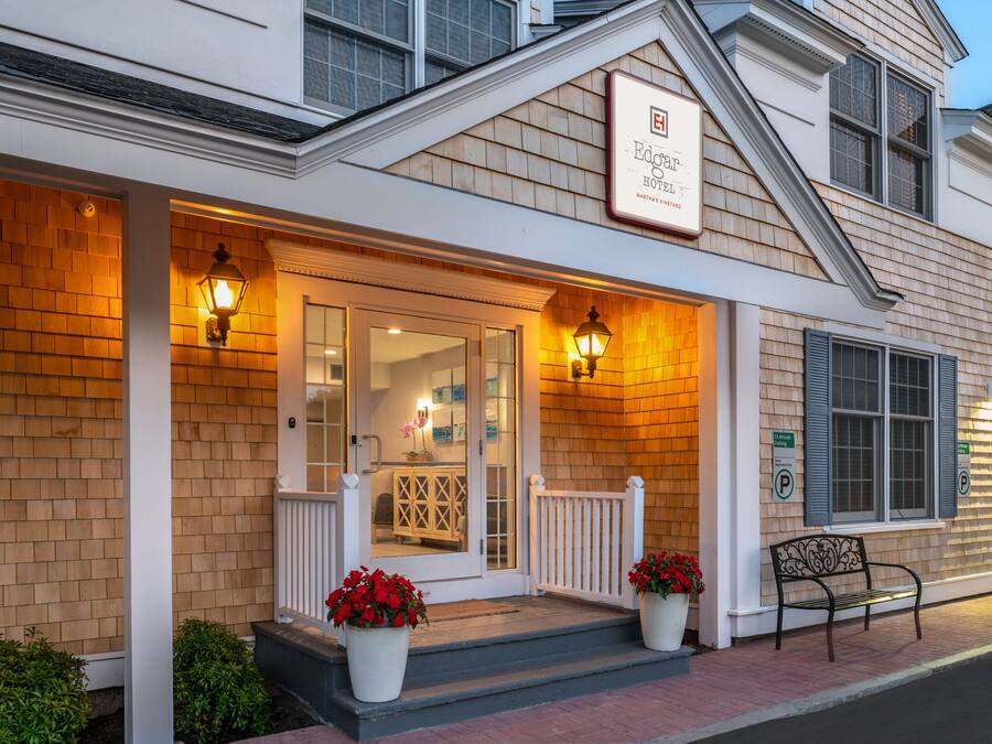 A hotel entrance with a brick facade, a white porch, and a bench.