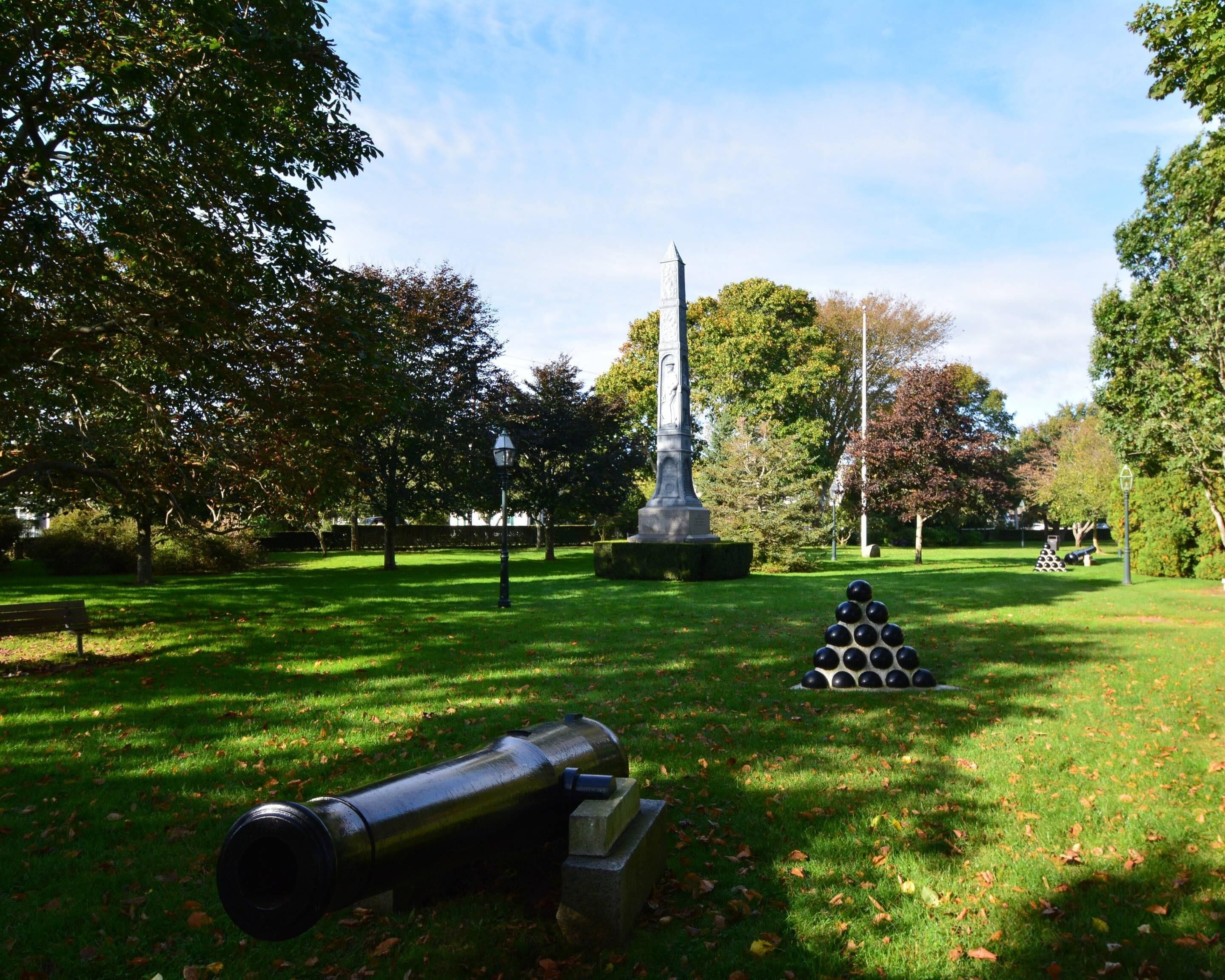 A park with a monument, a cannon, and a pyramid of balls.