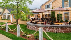 A brick patio with outdoor seating and umbrellas, surrounded by a landscaped garden and a building with blue shutters. - Edgar Hotel Martha's Vineyard, an Ascend Collection Hotel (Edgartown)