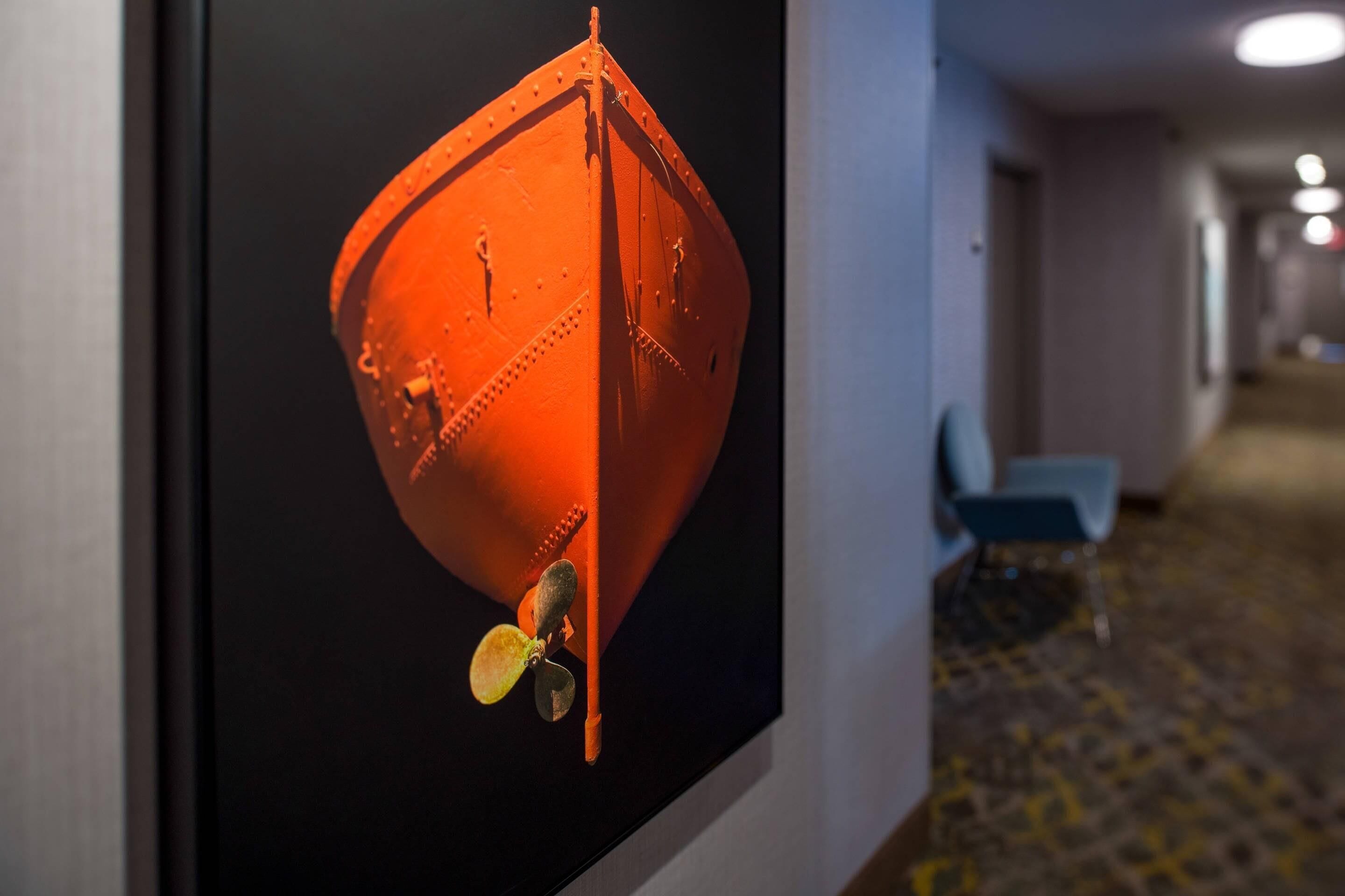 Un couloir orné d’une affiche représentant un objet sphérique, avec une chaise bleue et un tapis à motifs.