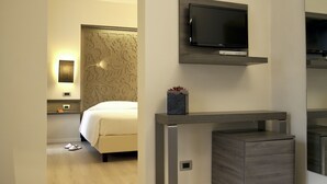 A modern hotel room with a bed, a TV mounted on the wall, a bedside table with a plant, and a wooden floor. - Hotel Diplomatic (Turin)
