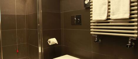 A modern bathroom with a glass-enclosed shower, a bidet, and a towel rack with multiple towels.