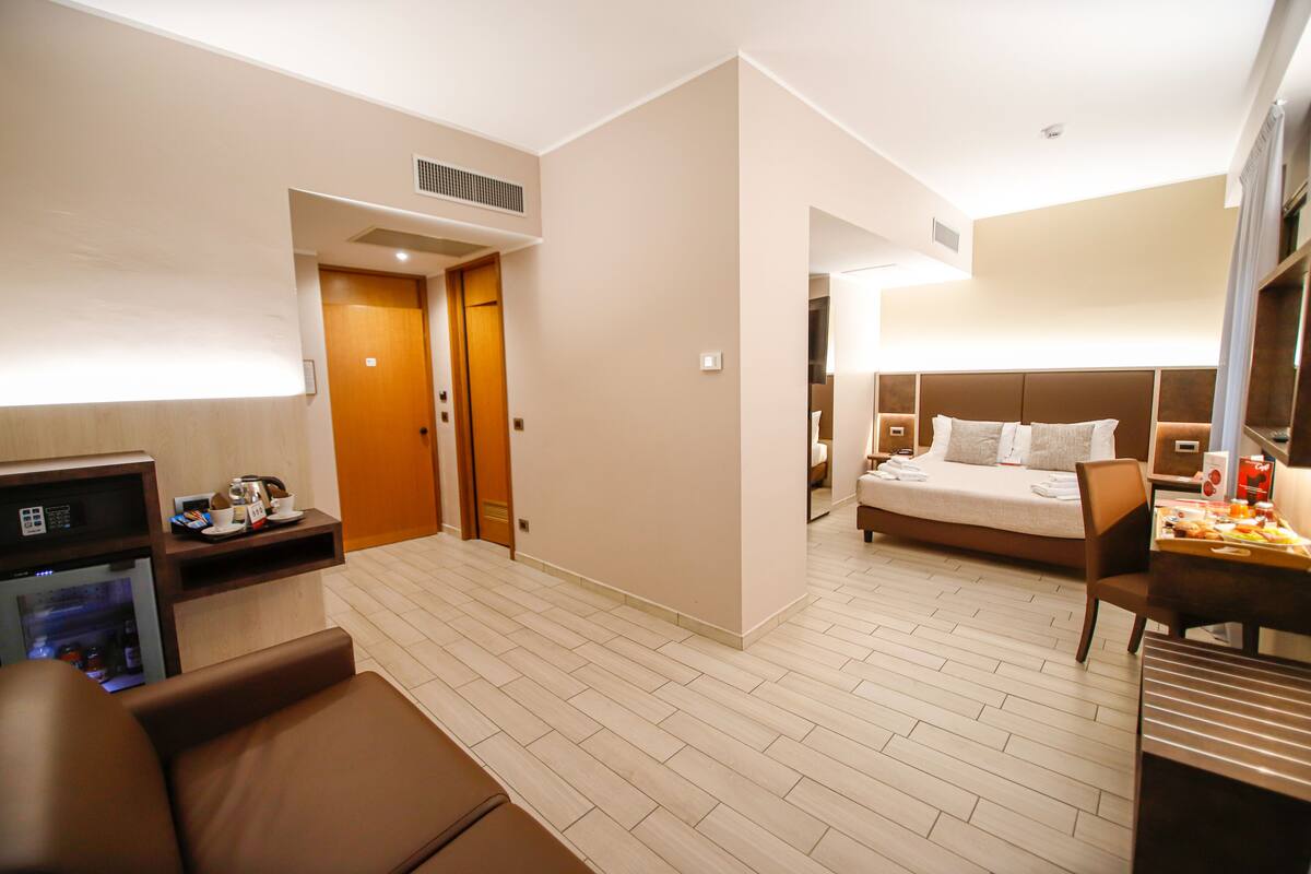 A hotel room with a bed, a desk, a chair, a small kitchenette, and a bathroom.