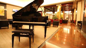 A grand piano in a well-lit lobby with a polished floor, comfortable seating, and a large window. - Hotel Diplomatic (Turin)