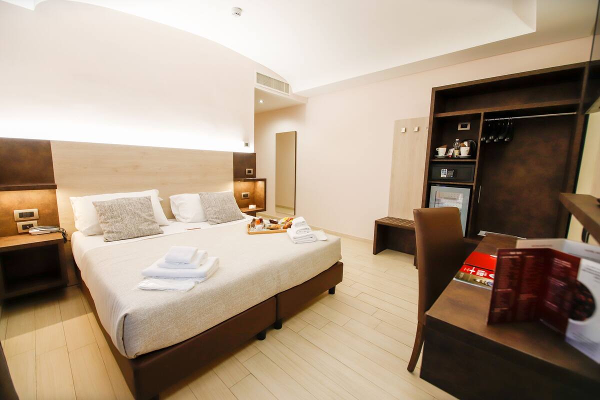 A modern hotel room with a large bed, bedside tables, a desk, and a wardrobe.