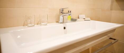 A white bathroom sink with a chrome faucet, two clear glasses, and a yellow soap dispenser.