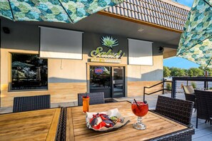 An outdoor seating area with a table set for two, a menu board, and a building with a sign reading 'Salud! BAR & KITCHEN'. - Richland Riverfront Hotel and Conference Center, Ascend Hotel Collection (Richland)