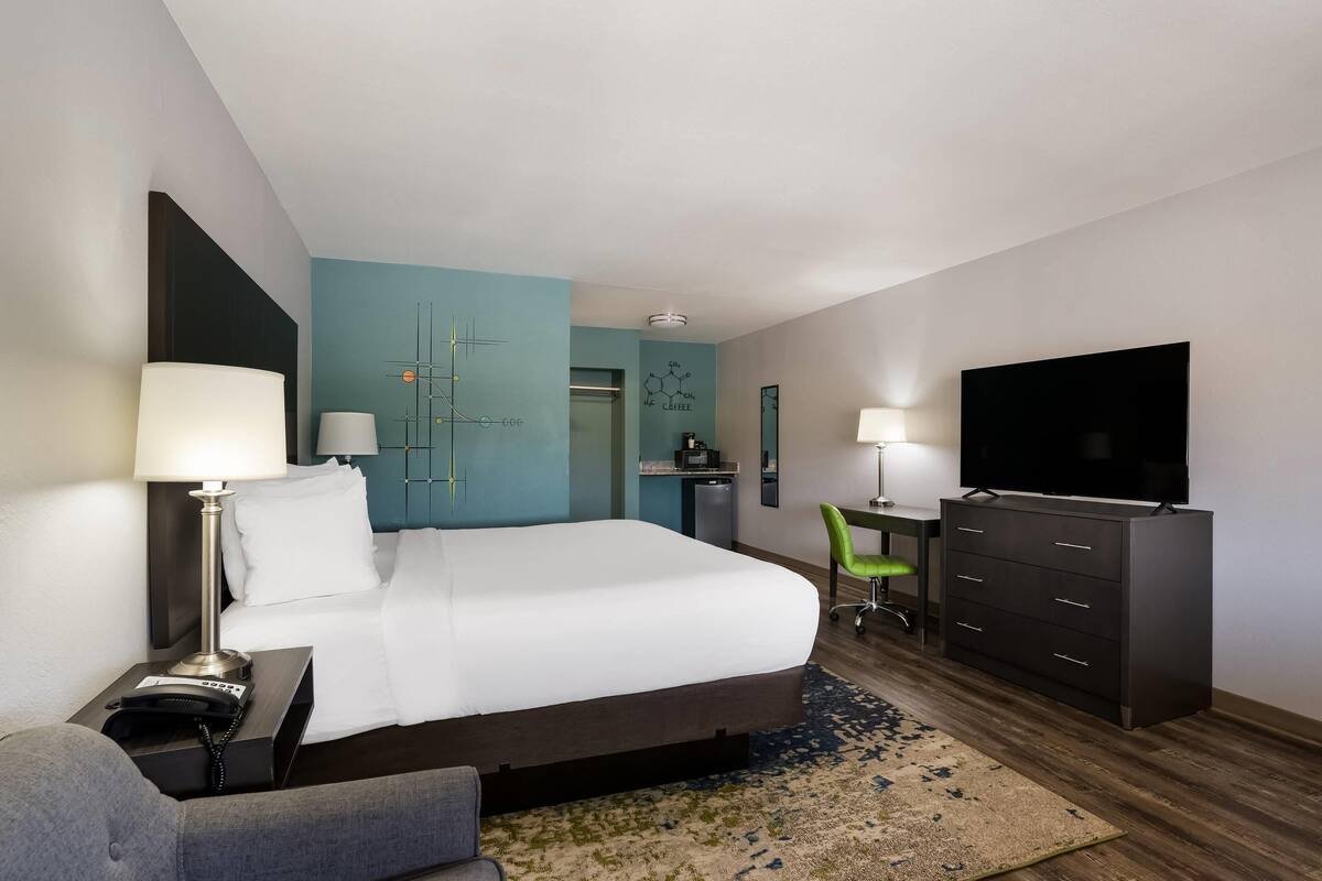 Ein Hotelzimmer mit Bett, Nachttischen, einem Schreibtisch mit Stuhl, einem Fernseher und einer Kaffeemaschine.