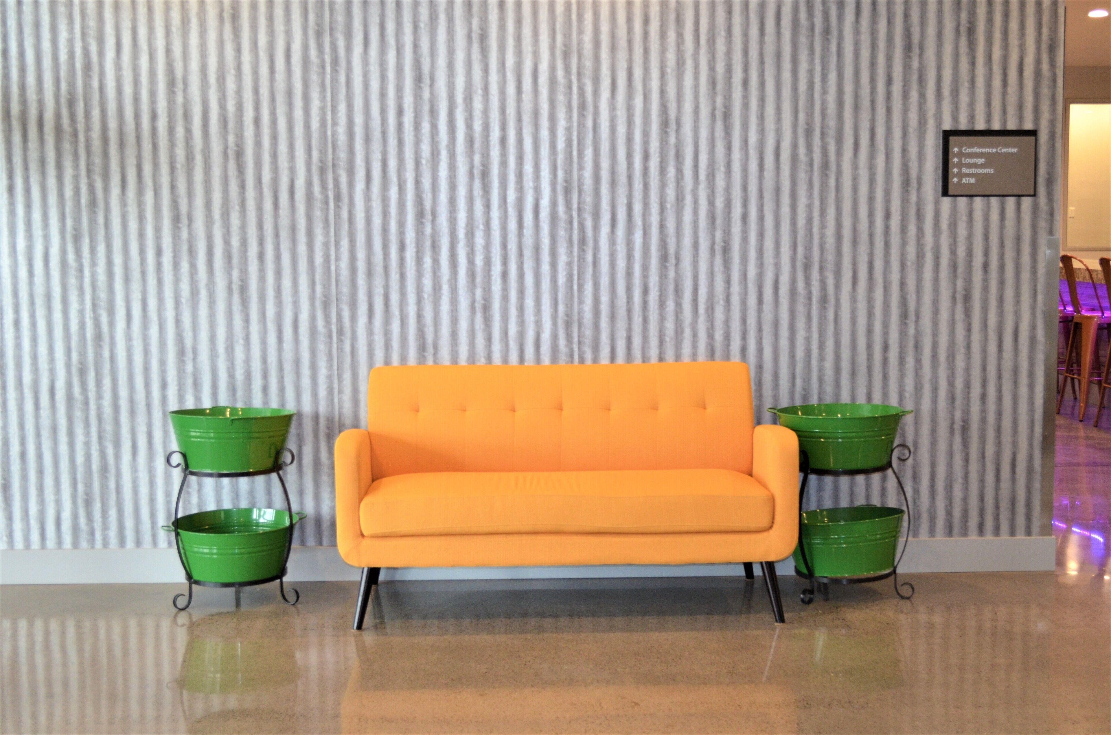 A modern hotel lobby with a striped wall, a bright orange sofa, and green planters.