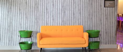 A modern hotel lobby with a striped wall, a bright orange sofa, and green planters.