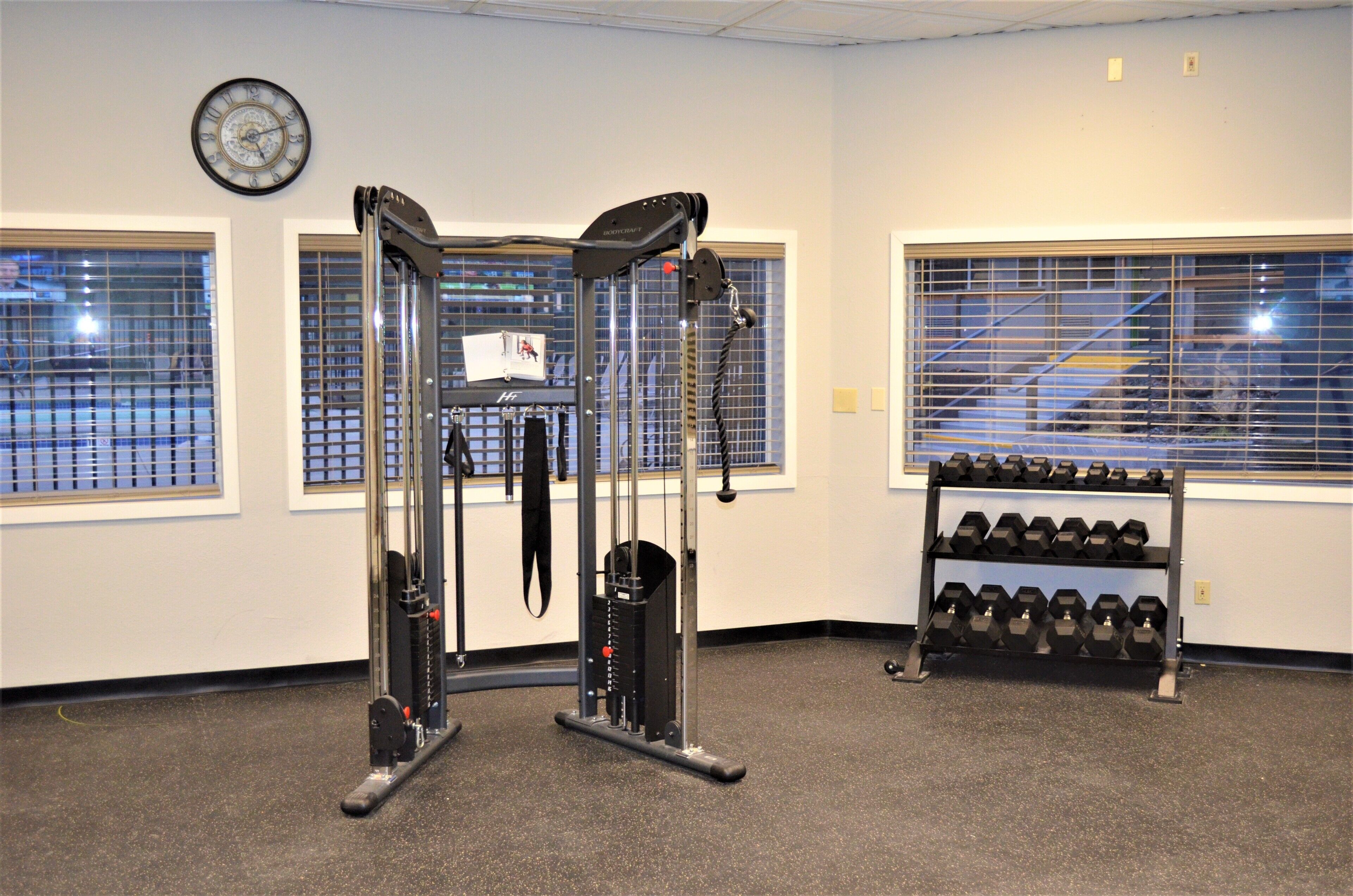 A gym with exercise equipment, a clock, and a rack of dumbbells.