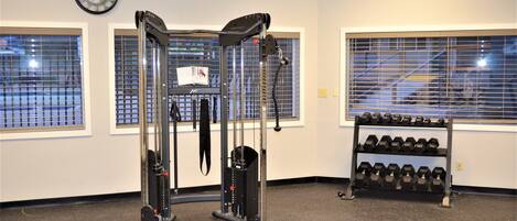 A gym with exercise equipment, a clock, and a rack of dumbbells.