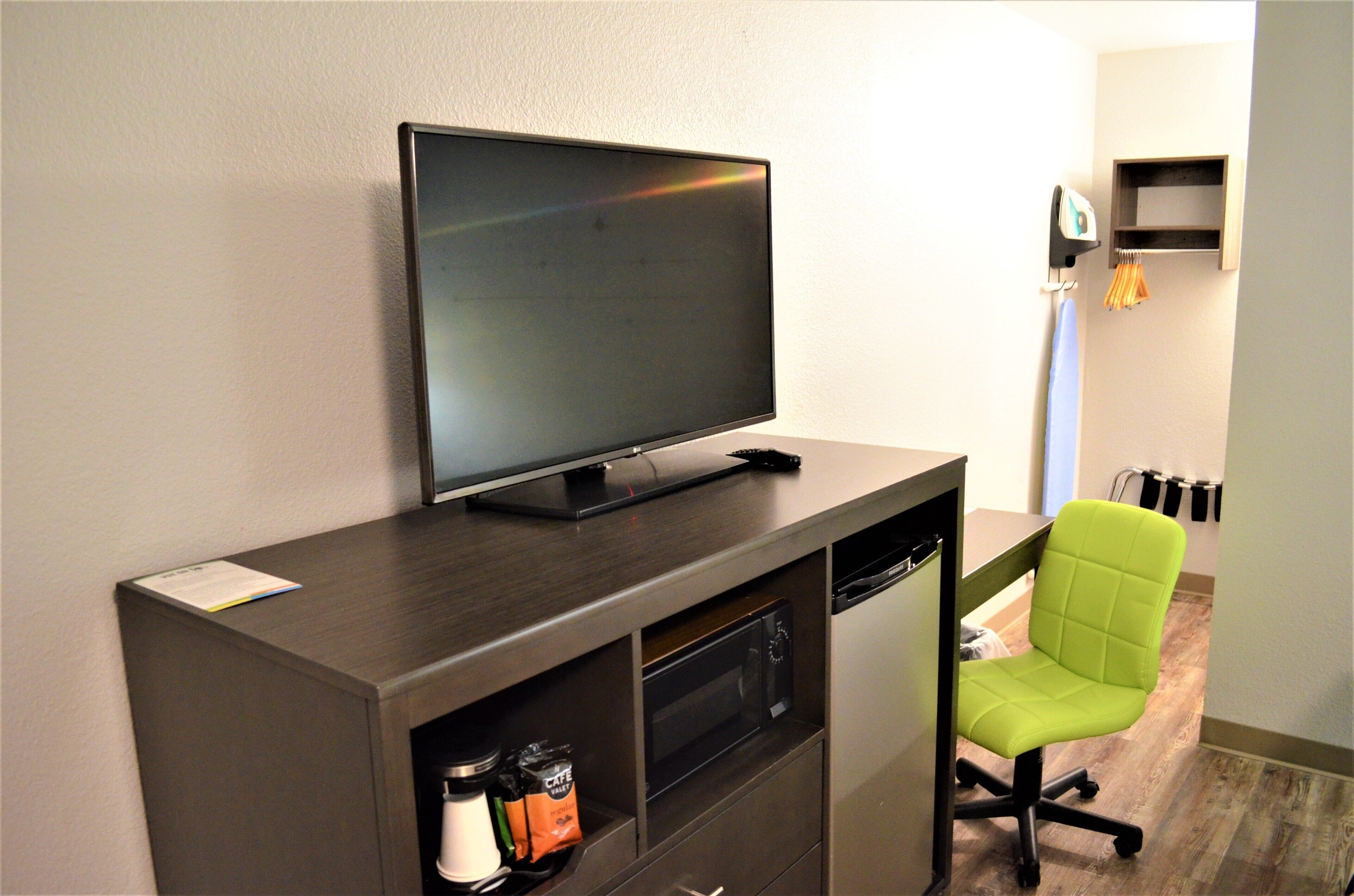 Ein modernes Hotelzimmer mit einem Flachbildfernseher auf einer Holzkonsole, einem grünen Bürostuhl und einer Mikrowelle.