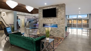 A modern lobby with a green sofa, a flat-screen TV mounted on a stone wall, a reception desk, and a staircase. - Richland Riverfront Hotel and Conference Center, Ascend Hotel Collection (Richland)