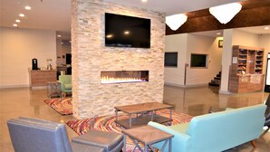 A modern living room with a stone wall, a flat-screen TV, a fireplace, and a sofa. - Richland Riverfront Hotel and Conference Center, Ascend Hotel Collection (Richland)