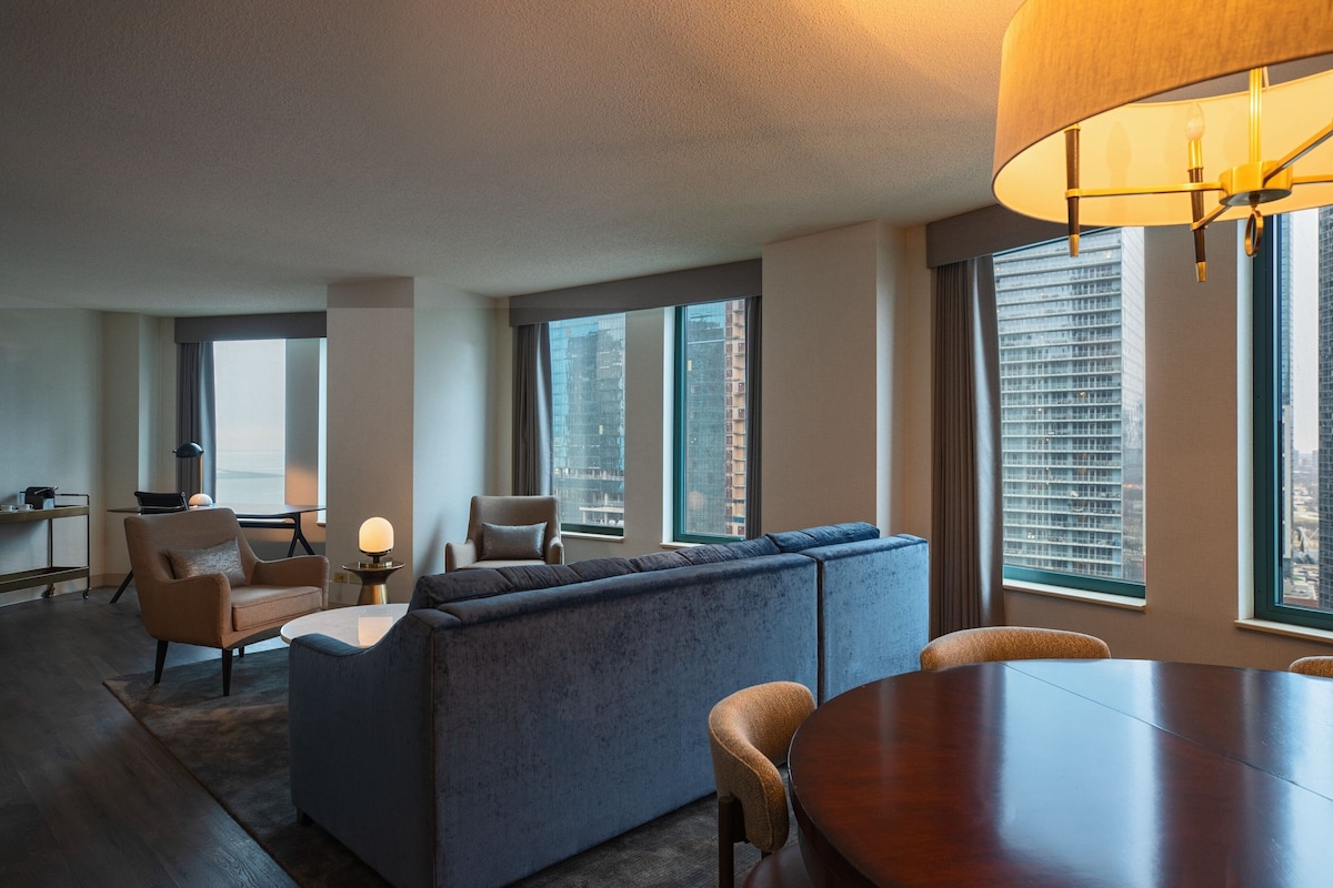 Una sala moderna con un sofá modular, una mesa de comedor y ventanas amplias con vistas a la ciudad.