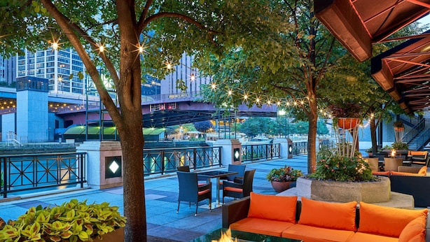 An outdoor seating area with a glass table, orange cushions, and potted plants. - Sheraton Grand Chicago Riverwalk (Chicago)