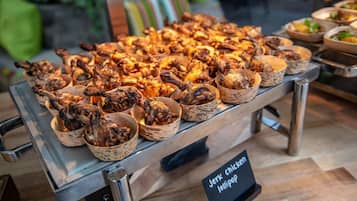Une table de buffet proposant divers plats, notamment du poulet à la sauce jerk et des brochettes.