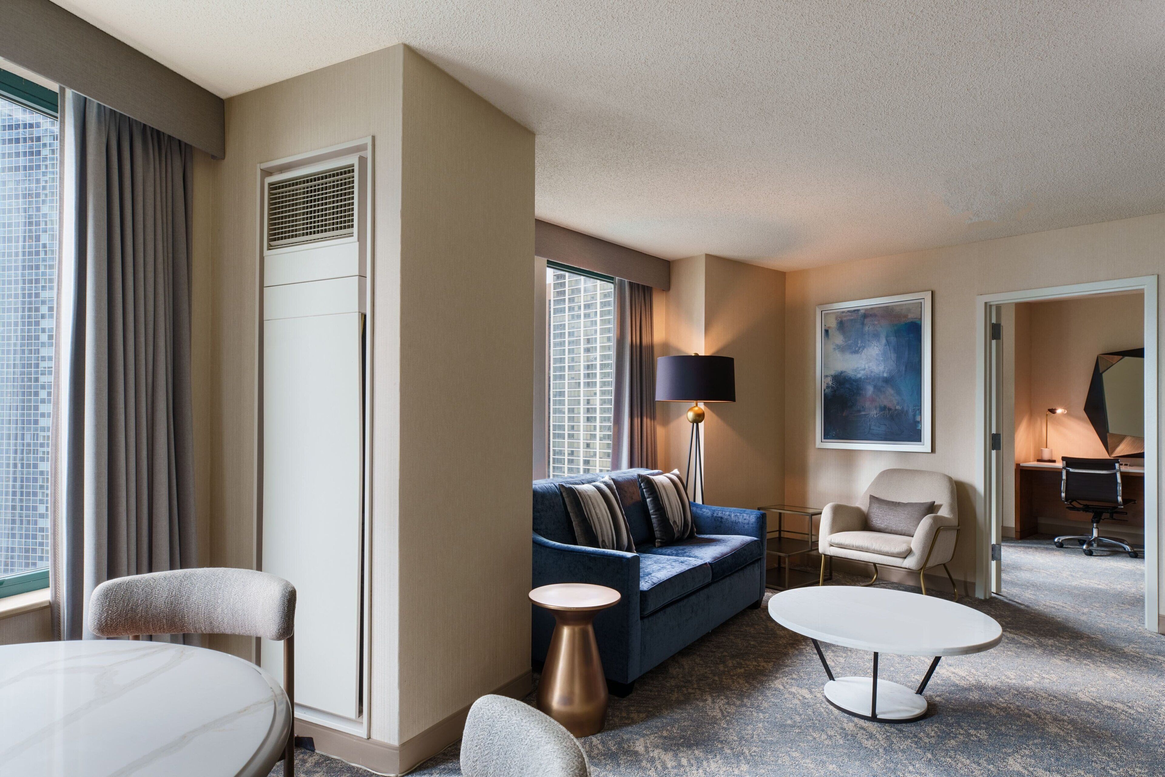 A hotel room with a sofa, armchair, round table, and a lamp.