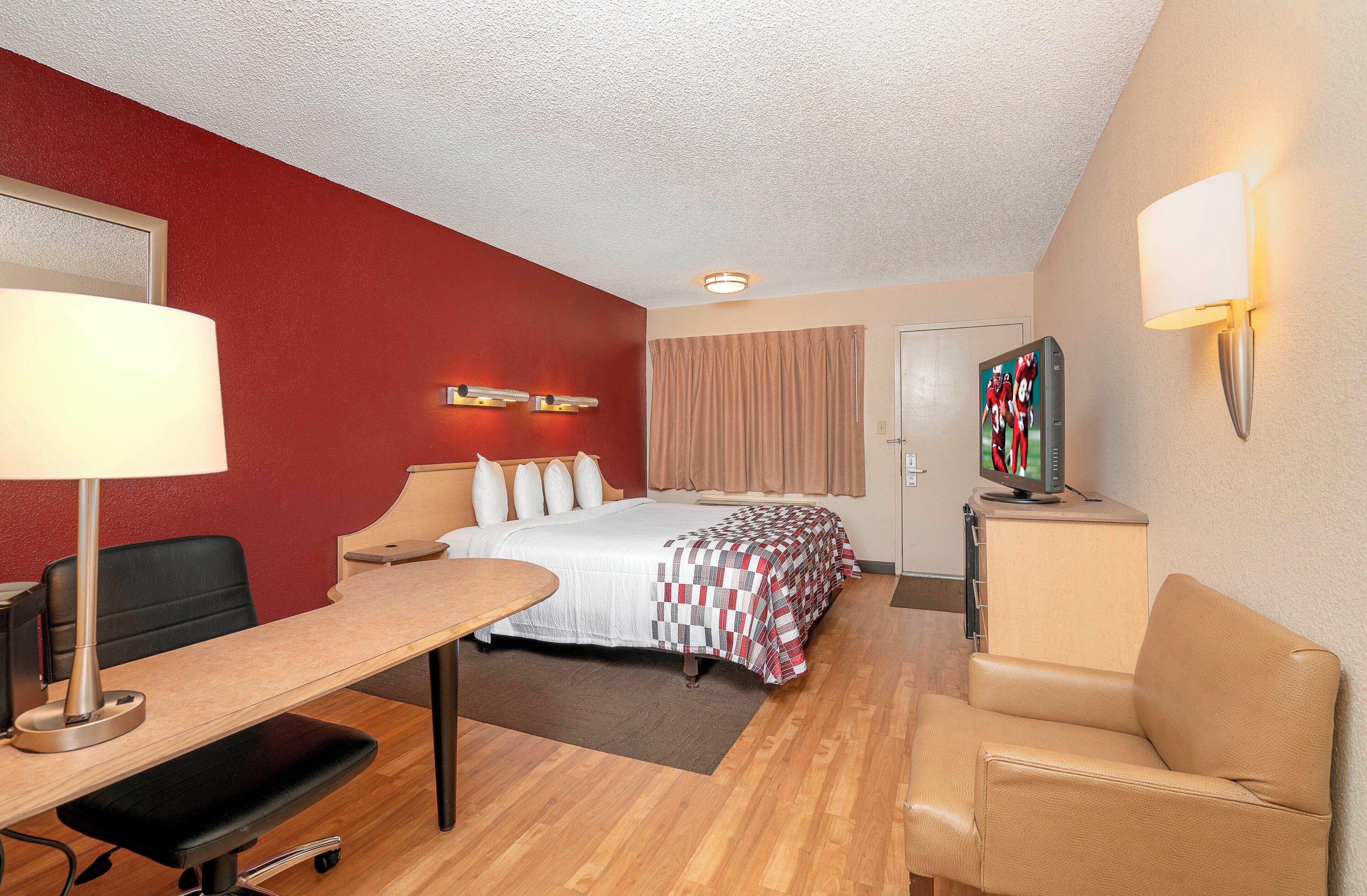 Ein Hotelzimmer mit Bett, Schreibtisch, Stuhl und Fernseher auf einem Standfuß.
