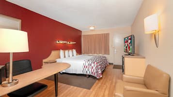 Una habitación de hotel con cama, escritorio, silla y televisor sobre un mueble.