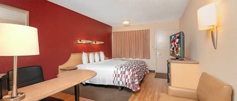 Une chambre d’hôtel équipée d’un lit, d’un bureau, d’une chaise et d’un téléviseur posé sur un meuble.