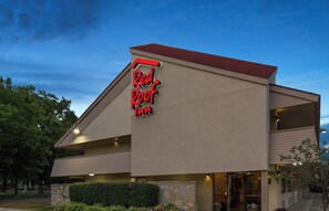Un hotel Red Roof Inn con un diseño arquitectónico moderno, que presenta un llamativo letrero de neón rojo, fachada de piedra y techo plano.