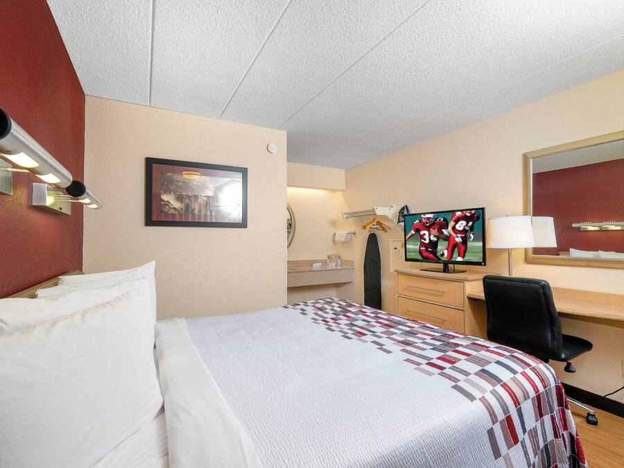 A hotel room with a bed, a desk with a computer, a TV, and a mirror.