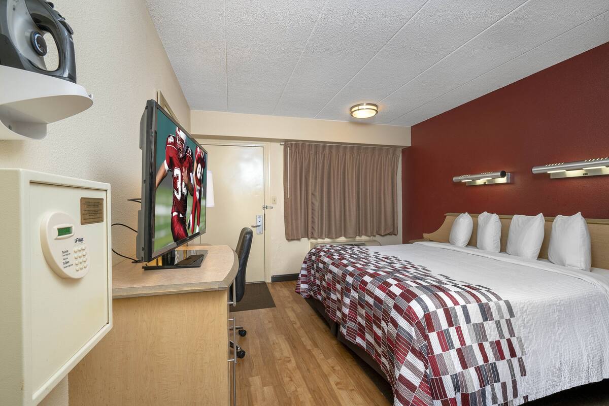 A hotel room with a bed, a desk with a computer, a television, and a control panel.