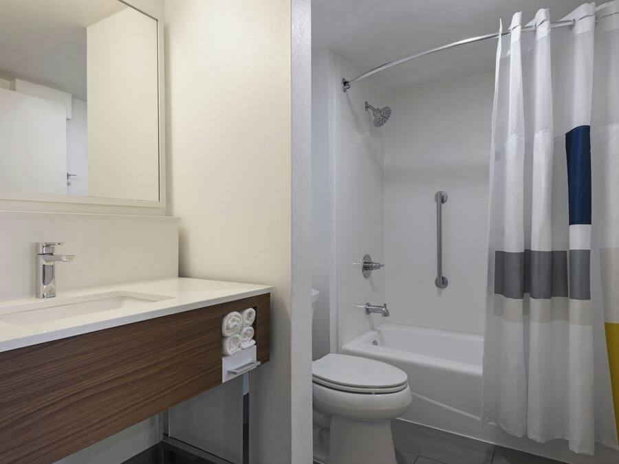 Een badkamer met een witte wasbak, een spiegel, een toilet en een douche met een gebogen glazen deur.