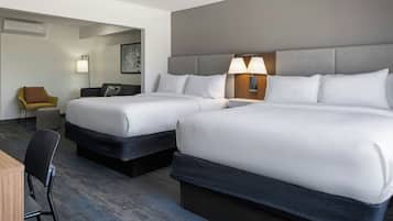 A hotel room with two beds, a desk, a chair, and a lamp.