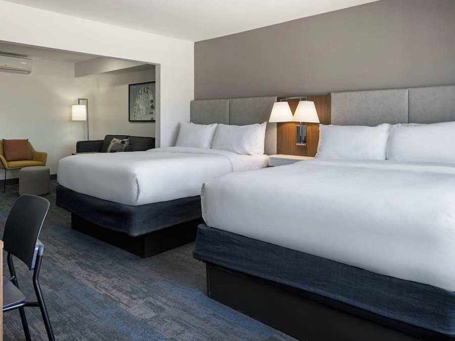 A hotel room with two beds, a desk, a chair, and a lamp.