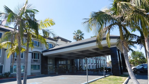 A modern hotel with a covered entrance, palm trees, and a parking lot.