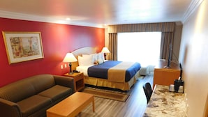 A hotel room with a bed, a sofa, a small table, a desk, and a painting on the wall.