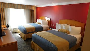 A hotel room with two beds, a desk, and a window with curtains.