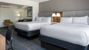A hotel room with two beds, a desk, a chair, a lamp, and a painting on the wall.