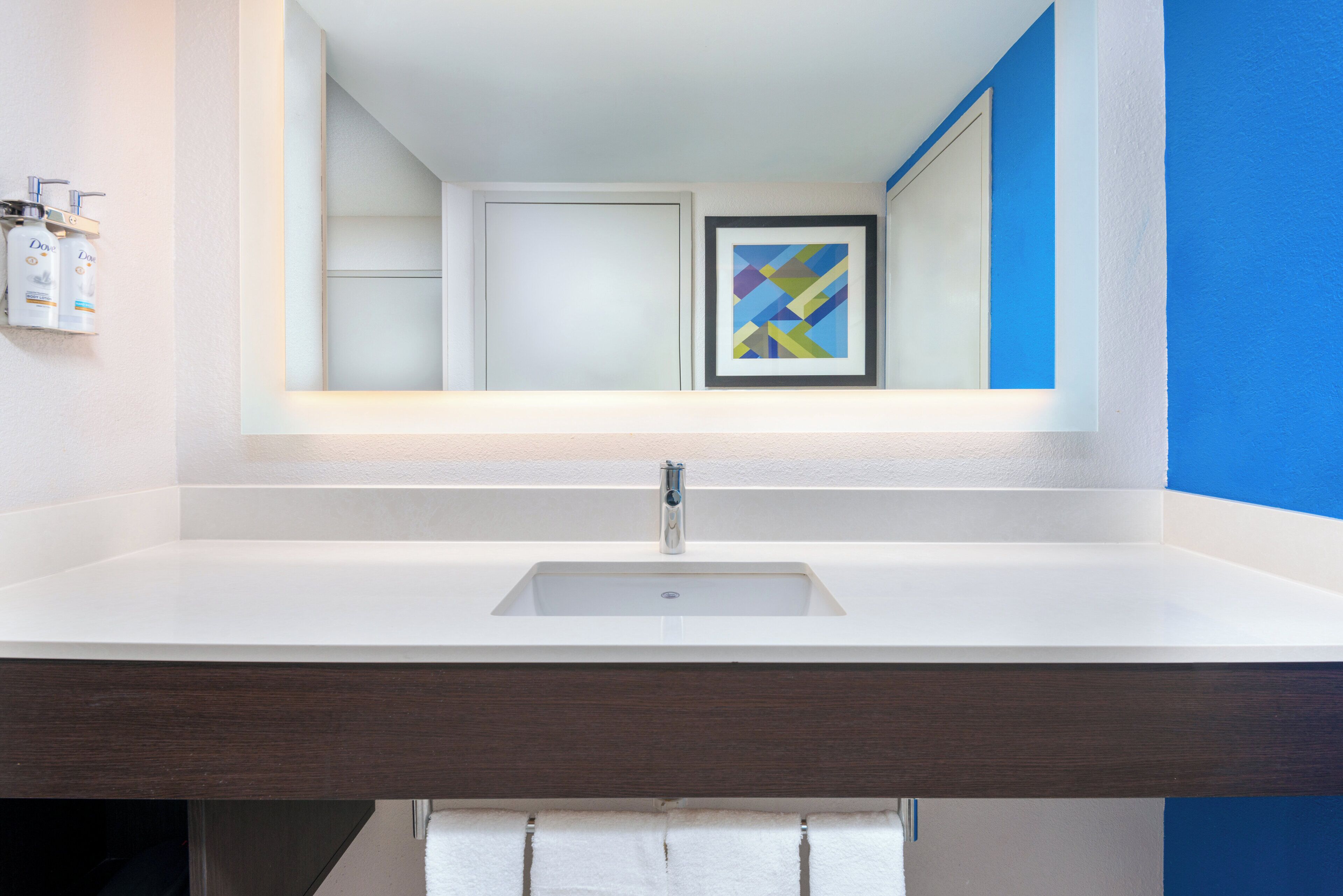A bathroom with a white sink, a framed abstract painting, and a blue accent wall.