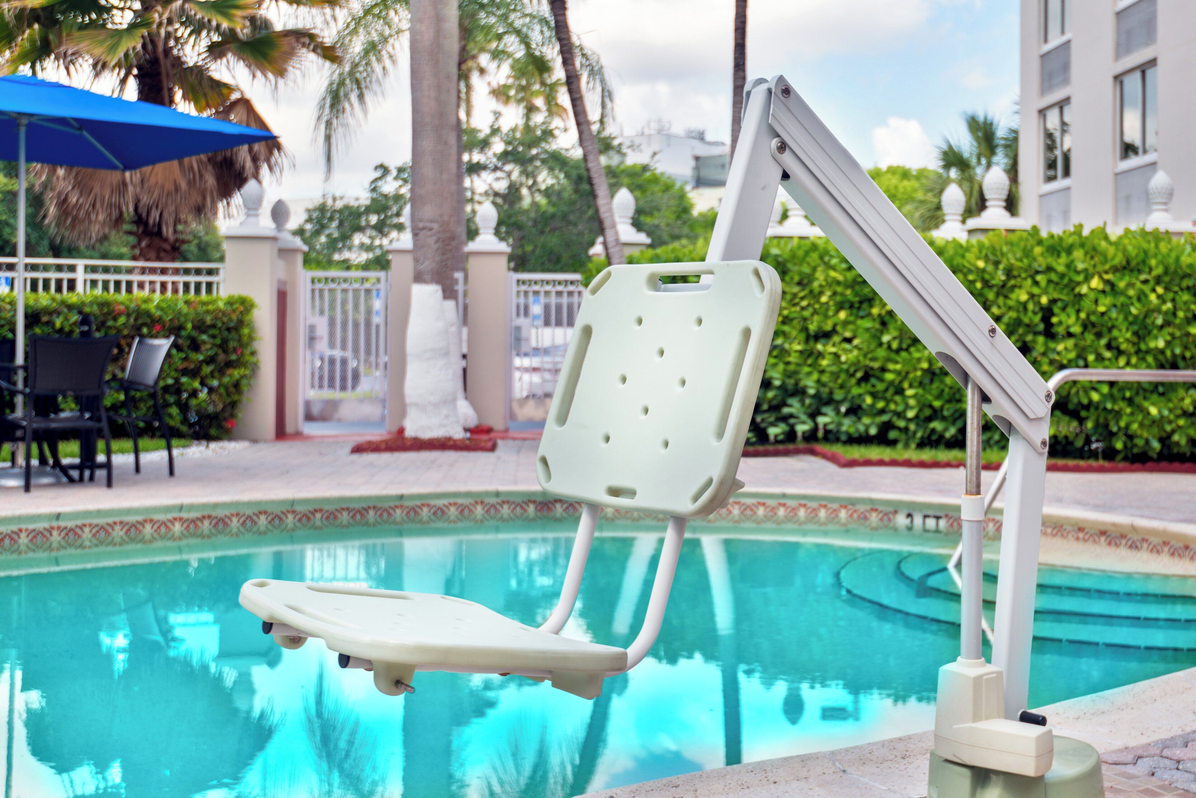 Una silla junto a la piscina, con una palmera y una valla al fondo.