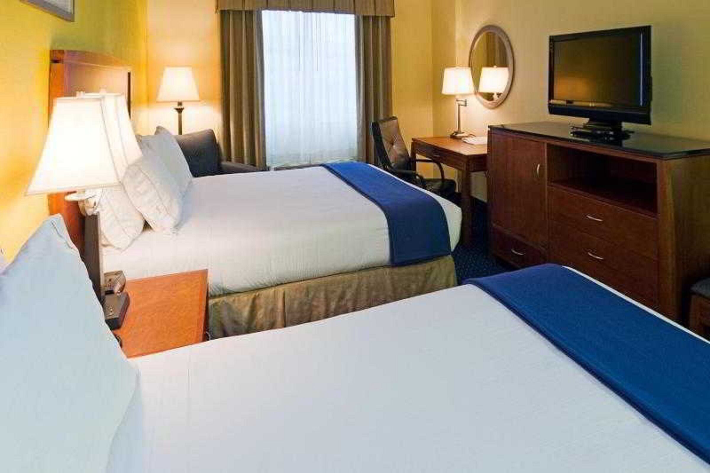 A hotel room with two beds, a desk with a chair, a television, and lamps.