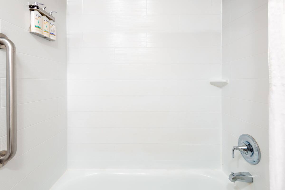A bathroom with white tiled walls, a shower, and a toilet.