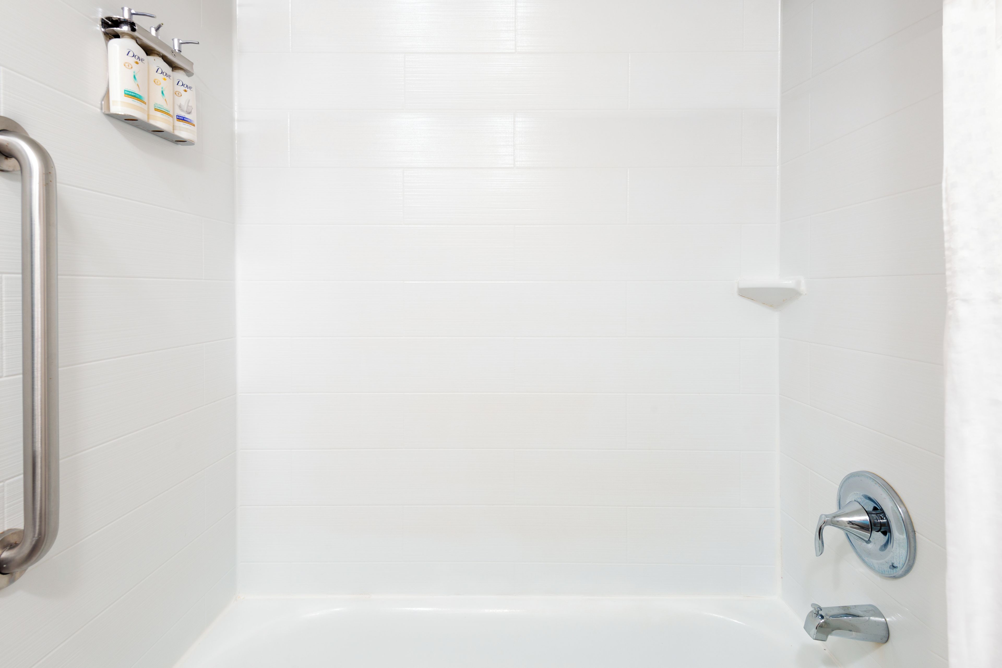 A bathroom with white tiles, a bathtub, a shower, and a handrail.