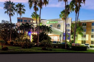 Un hotel Holiday Inn Express con facciata moderna, circondato da palme e curato giardino.