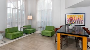 A modern living room with green sofas, a glass dining table, and a colorful artwork on the wall. - Holiday Inn Express Miami Airport Doral Area by IHG (Miami)