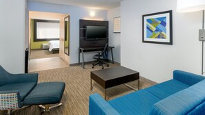 A hotel room with a TV, a desk, two blue sofas, a small table, and a bed with a window. - Holiday Inn Express Miami Airport Doral Area by IHG (Miami)