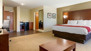Une chambre d’hôtel avec un grand lit, un bureau, une chaise, une petite kitchenette et un miroir.